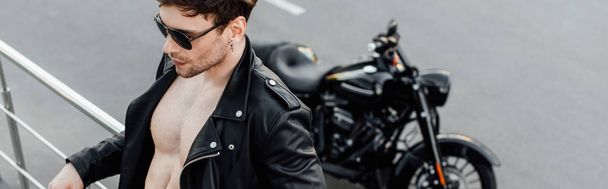 plano panorámico de hombre en chaqueta de cuero con torso desnudo apoyado en valla de metal de pie no muy lejos de la motocicleta
 - Foto, imagen