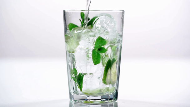 fresh water pouring in glass with slices lime, mint and ice cubes on white  - Footage, Video