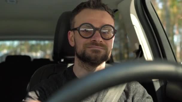 Задоволений бородатий чоловік в окулярах водить машину по вулиці в сонячну погоду
 - Кадри, відео