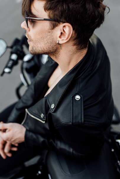 selective focus of young man in leather jacket sitting on motorcycle with closed eyes - Фото, зображення