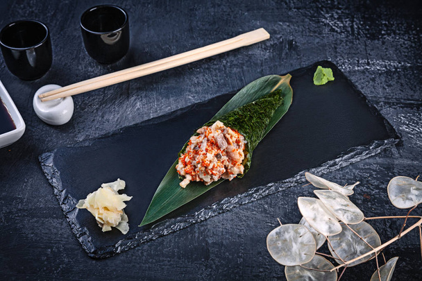 Close-up of tasty hand roll sushi with eel and Tobico caviar served on dark stone plate with soy sauce and ginger. Copy space. Temaki, Japanese cuisine. Healthy food - Foto, Bild