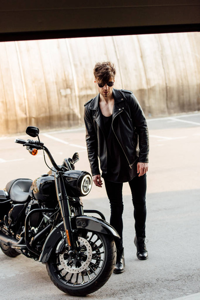 joven guapo caminando al garaje a la motocicleta negro
 - Foto, Imagen