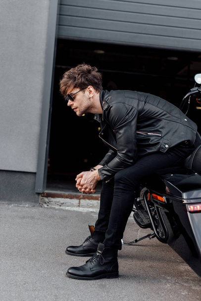 oldalnézetből jóképű férfi bőrdzseki ül a fekete motorkerékpár  - Fotó, kép