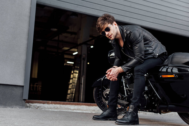 joven guapo sentado en motocicleta sentado cerca de garaje abierto
  - Foto, Imagen
