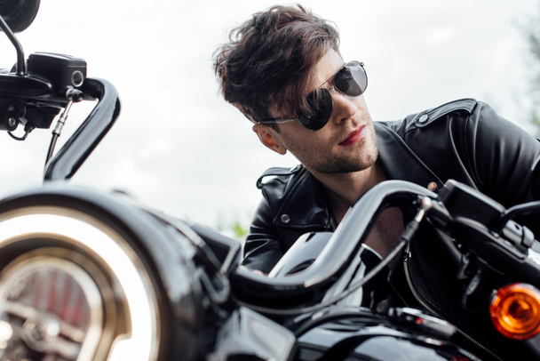 selective focus of lighting up lamp and handsome man sitting on motorcycle and looking away - Foto, Imagem