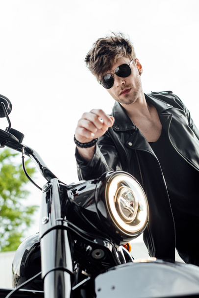 low angle view of handsome motorcyclist standing near motorcycle and leaning on handlebars - 写真・画像