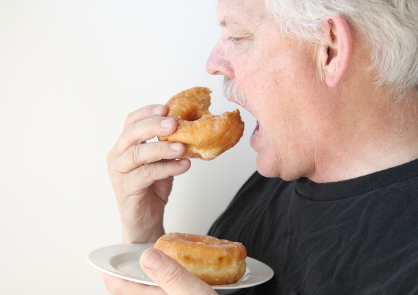 年上の男は、艶をかけられたドーナツを食べる - 写真・画像