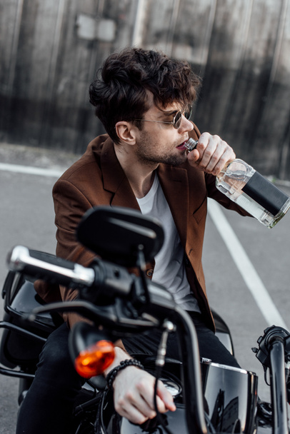 selective focus of handsome man drinking alcohol while sitting on motorcycle - Photo, Image