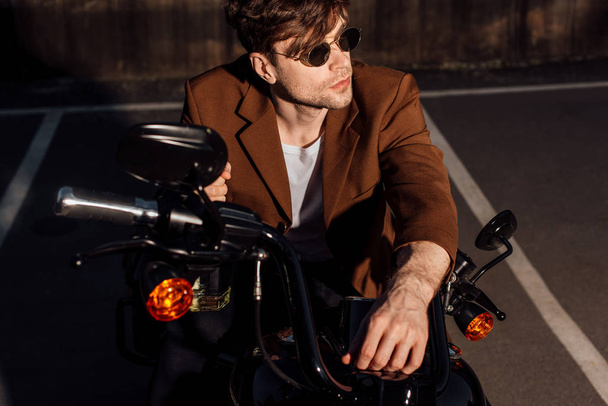 handsome man in sunglasses sitting on motorcycle and looking away - Φωτογραφία, εικόνα