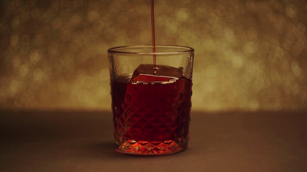 whiskey pouring in glass with big frozen ice cube on brown  - Záběry, video