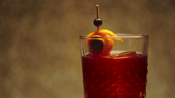 toothpick with orange peel and black currants in spinning alcohol drink on brown  - Footage, Video