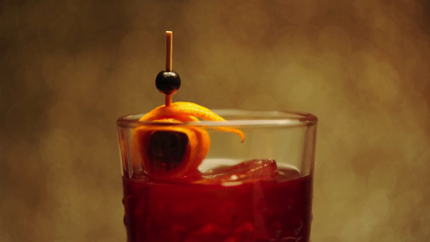 toothpick with orange peel in spinning alcohol drink on brown  - Footage, Video