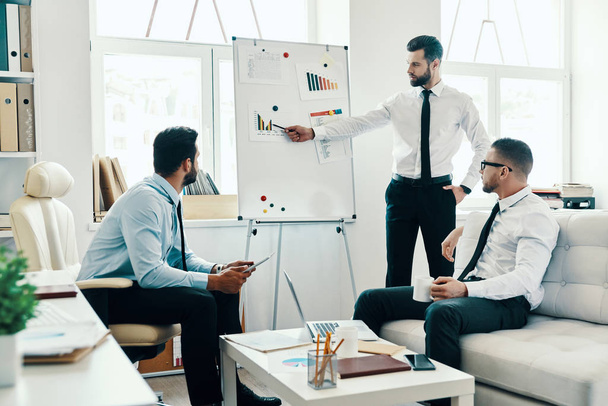 Developing new strategy, businessmen in formalwear conducting a business presentation using flipchart while working in office       - Фото, зображення