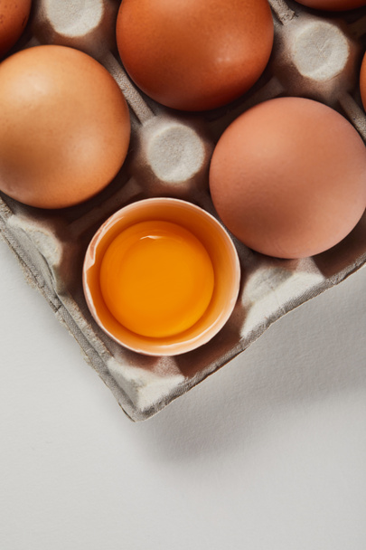  a törött tojáshéj és a sárga sárgája felülnézete a kartondobozban található tojások mellett - Fotó, kép