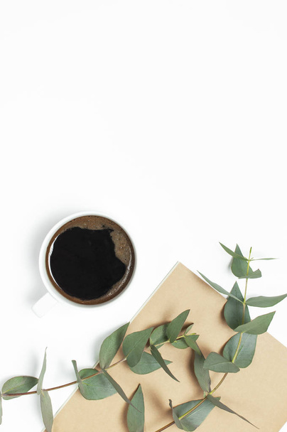 Cup of black coffee, notebook, diary, pens, green sprig of eucalyptus on white background. Flat lay, top view, copy space. Feminine desk workspace, morning breakfast, hot drink, coffee background - Photo, Image