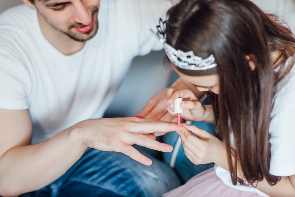 Handsome young man at home with little cute girl doing nails   - Foto, Bild