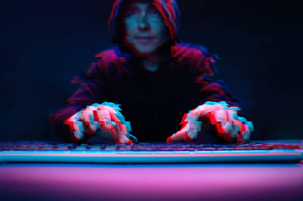 Hacker in the hood working with computer typing text in dark room. Image with glitch effect - Photo, Image