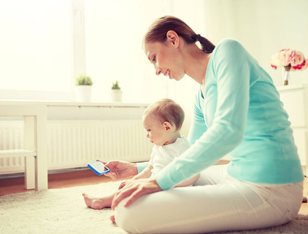 happy mother showing smartphone to baby at home - Photo, Image