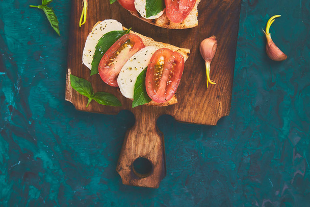 Caprese Bruschetta toast op snijplank. Bruschetta met tomaten, mozzarella kaas en basilicum op een groene achtergrond. Traditionele Italiaanse aperitief of snack, Antipasto - Foto, afbeelding