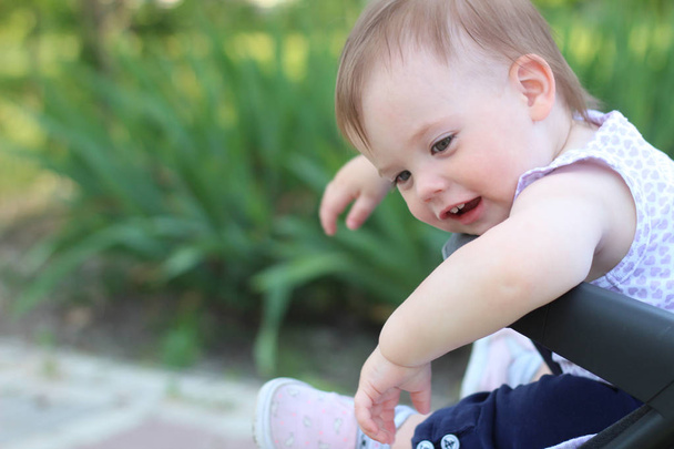 pequeño, hermoso, sonriente, lindo bebé pelirrojo en un cochecito al aire libre en una camisa sin mangas mirando hacia abajo
 - Foto, imagen