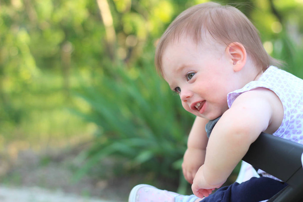 kleines, schönes, lächelndes, niedliches rothaariges Baby im Kinderwagen draußen im ärmellosen Hemd, das nach unten schaut - Foto, Bild