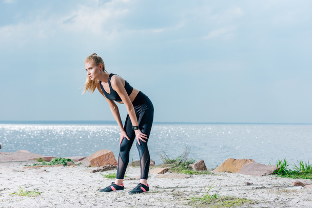 attractive and tired sportive woman standing on beach near sea  - Valokuva, kuva