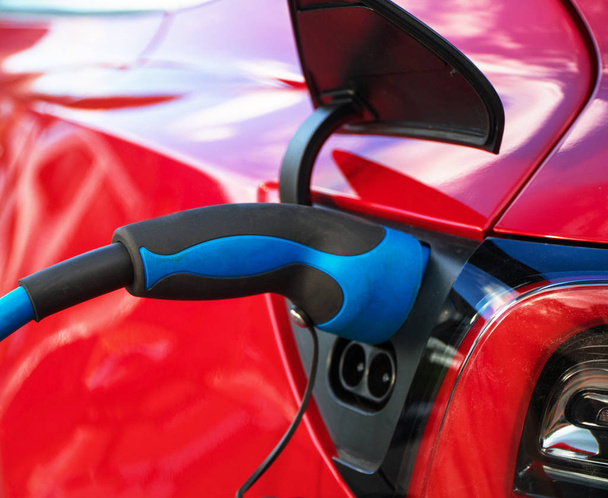 赤いスポーツ電気自動車を充電する電気プラグ. - 写真・画像