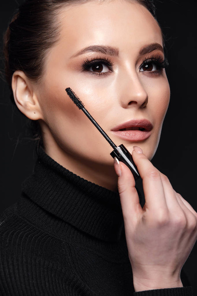Beauty Cosmetics.Woman applying black mascara on eyelashes with makeup brush. photos of appealing brunette girl on black background.High Resolution - Fotó, kép
