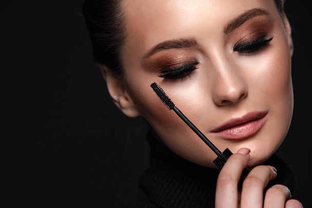Beauty Cosmetics.Woman applying black mascara on eyelashes with makeup brush. photos of appealing brunette girl on black background.High Resolution - 写真・画像