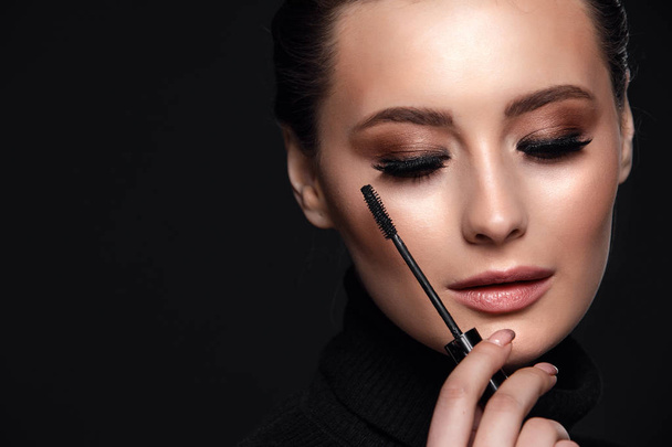 Beauty Cosmetics.Woman applying black mascara on eyelashes with makeup brush. photos of appealing brunette girl on black background.High Resolution - Фото, изображение