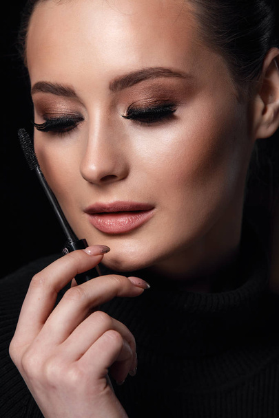 Beauty Cosmetics.Woman applying black mascara on eyelashes with makeup brush. photos of appealing brunette girl on black background.High Resolution - Foto, imagen