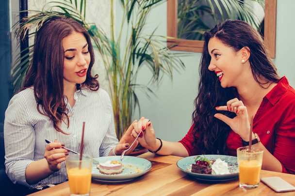 zwei schöne Mädchen genießen Saft und Kuchen zusammen in einem Café - Foto, Bild