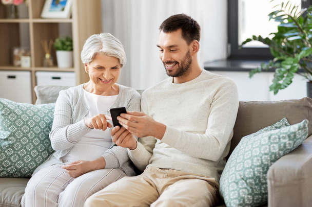 old mother and adult son with smartphone at home - Foto, Imagem