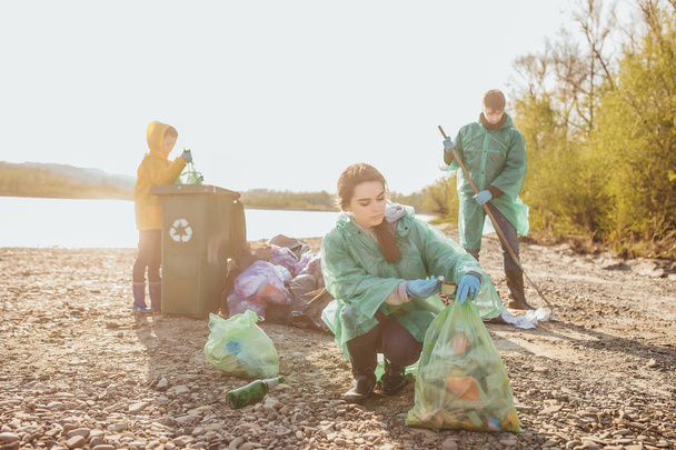 group of volunteers with garbage bags cleaning area near lake - Fotó, kép