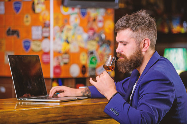 Businessman internet surfing drink alcohol. Man bearded businessman bar counter laptop cognac. Hipster freelancer work online drinking cognac. Pleasant relax successful businessman. Celebrate success - Fotó, kép