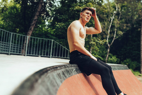 Athlete relaxing after training on workout ground outdoors. Handsome fit man looking away, taking a break after exercising outdoors. People and sport concept - Photo, image
