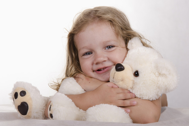 Two-year-old girl lies and bear hugs - Φωτογραφία, εικόνα