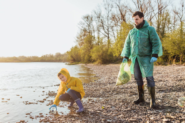 cute boy helping father to clean garbage near lake - Photo, image