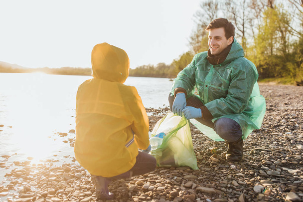 cute boy helping father to clean garbage near lake - Foto, afbeelding