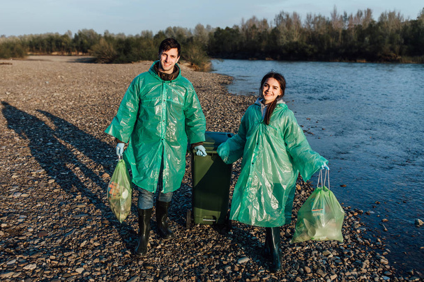 Man and woman volunteers with garbage for recycling near river - Photo, image