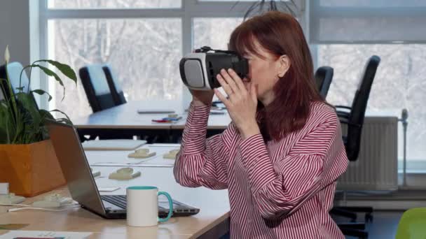 Mulher de negócios madura gostando de usar fone de ouvido realidade virtual em seu local de trabalho
 - Filmagem, Vídeo