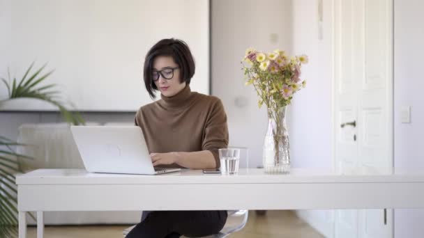 Asian woman in eyeglasses working with laptop in white home office - Metraje, vídeo