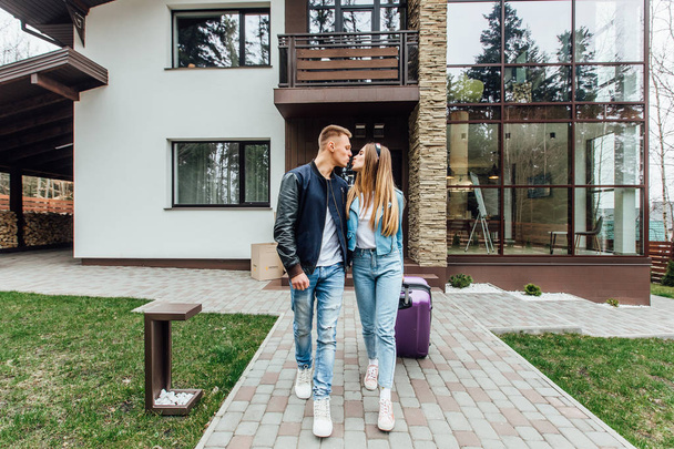 Two happy young people moving to new house with violet suitcase  - Fotoğraf, Görsel