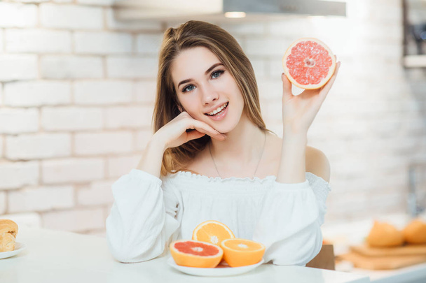 Young beauty woman having breakfast in kitchen with two grapefruits - Фото, зображення