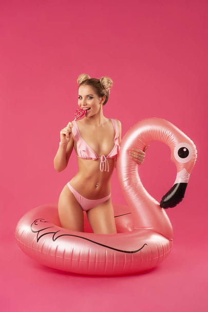 gyönyörű szőke egy fürdőruhát egy nyalóka a kezében, és egy felfújható flamingó  - Fotó, kép