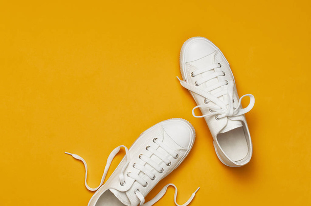 黄色のオレンジの背景に白い女性のファッションスニーカー。フラットレイトップビューコピースペース。女性の靴スタイリッシュな白いスニーカー。ファッションブログや雑誌のコンセプト。ミニマルな靴の背景、スポーツ - 写真・画像