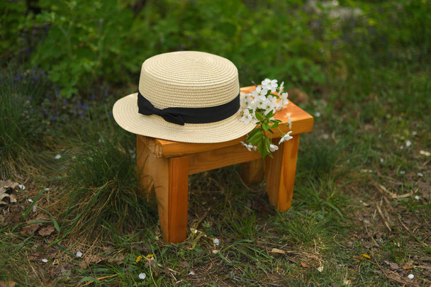 Słomkowy kapelusz na ławce w ogrodzie z wiśniowym kwiatami na trawie - Zdjęcie, obraz