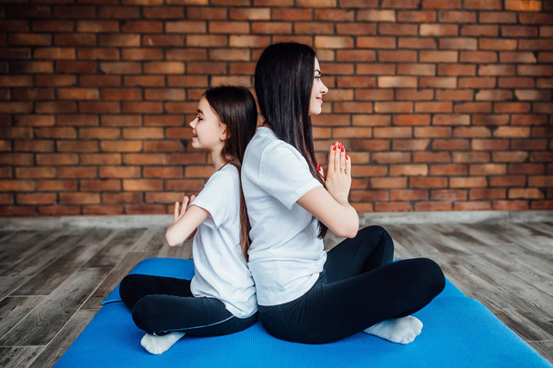 Young woman with daughter in sportswear practicing yoga - Fotoğraf, Görsel