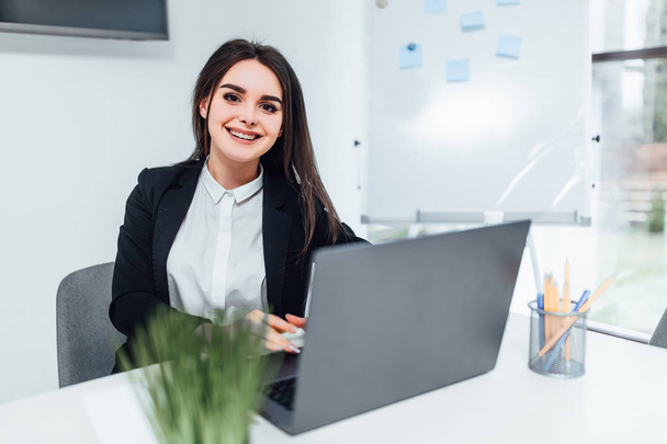 Smiling businesswoman sitting in modern office and using laptop - Φωτογραφία, εικόνα