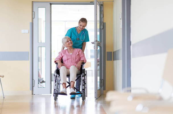 Ηλικιωμένη γυναίκα σε αναπηρικό καροτσάκι με νοσοκόμα στο νοσοκομείο - Φωτογραφία, εικόνα